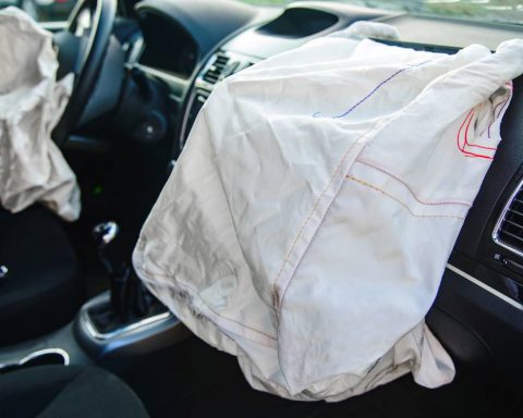 A luxury car with a faulty airbag system deployed and draped over the car's dash and console area.