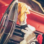 A man polishing the chrome edge of taillights on a classic car.