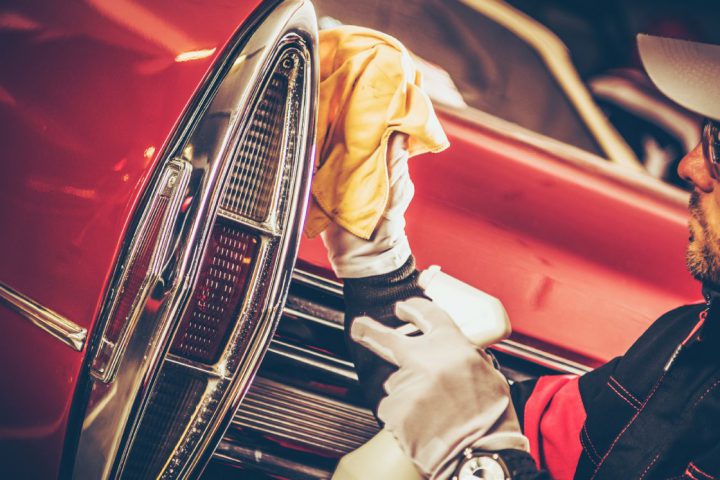 A man polishing the chrome edge of taillights on a classic car.