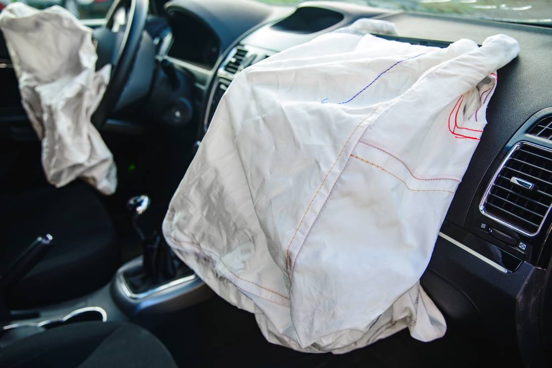 A luxury car with a faulty airbag system deployed and draped over the car's dash and console area.